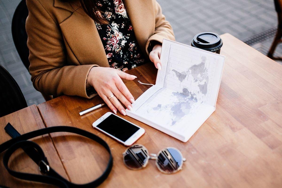 Voyageuse consultant un carnet de voyage, un smartphone et un café à une table