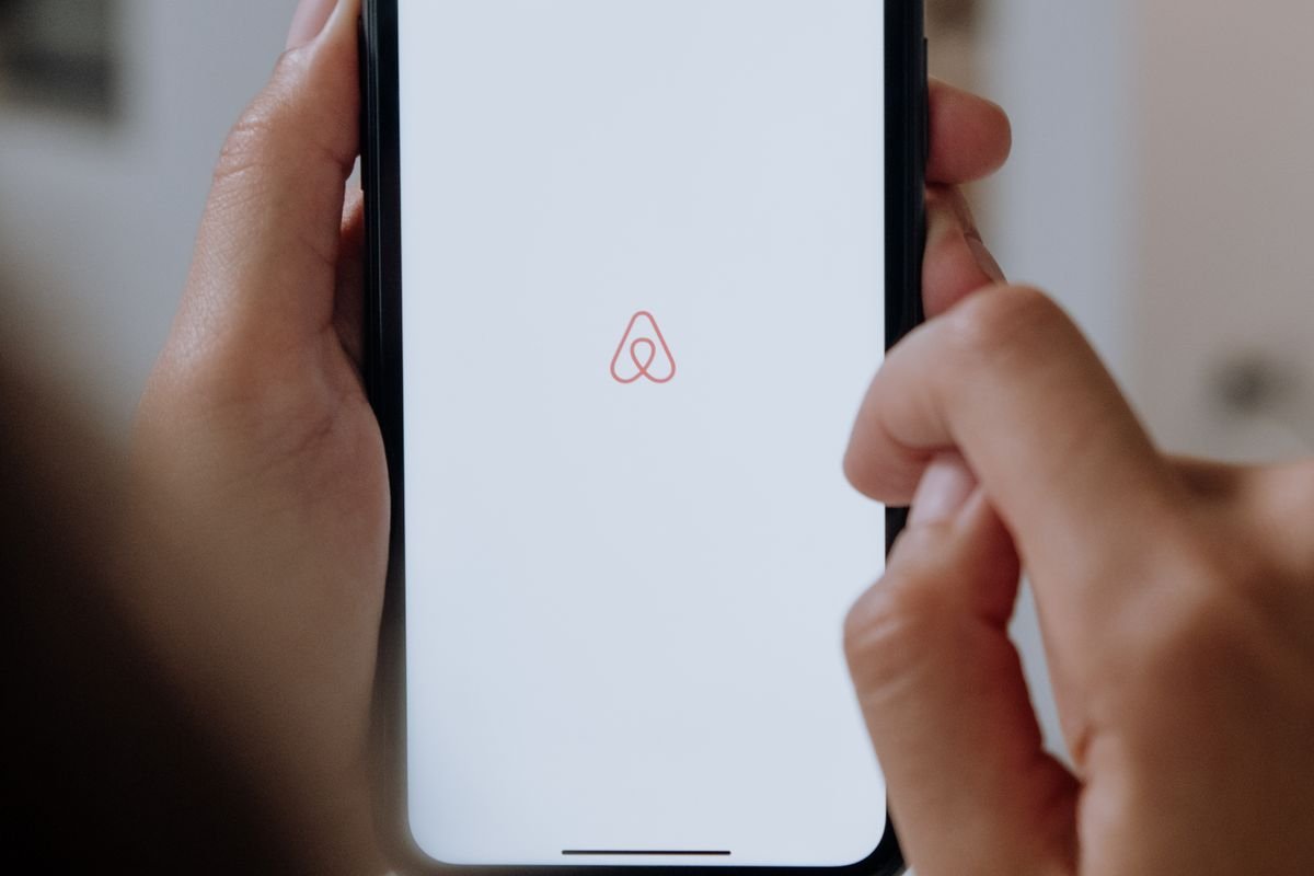 Mains tenant un smartphone affichant le logo Airbnb pour annuler une réservation