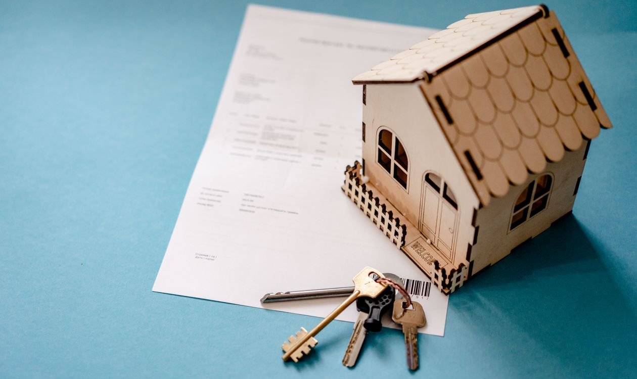 Maison miniature en bois posée sur un document administratif avec un trousseau de clés