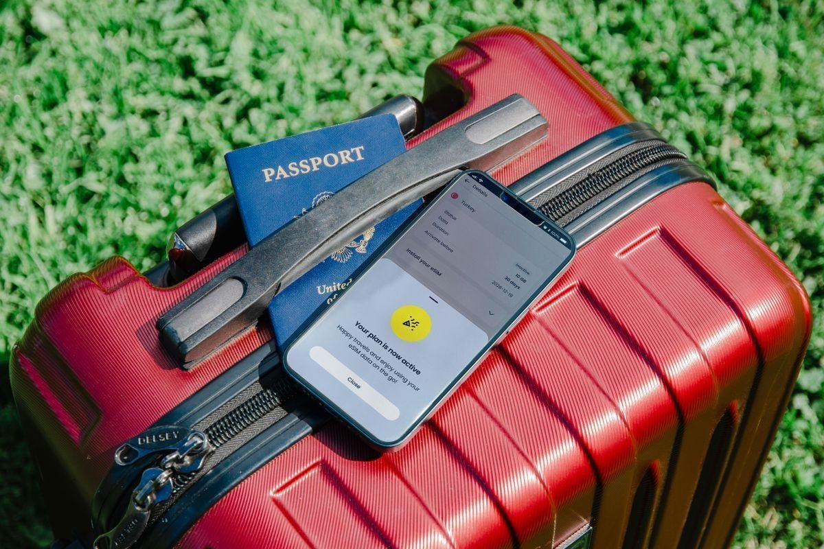 Valise de voyage, passeport et smartphone posés sur l'herbe, symbolisant un séjour annulé
